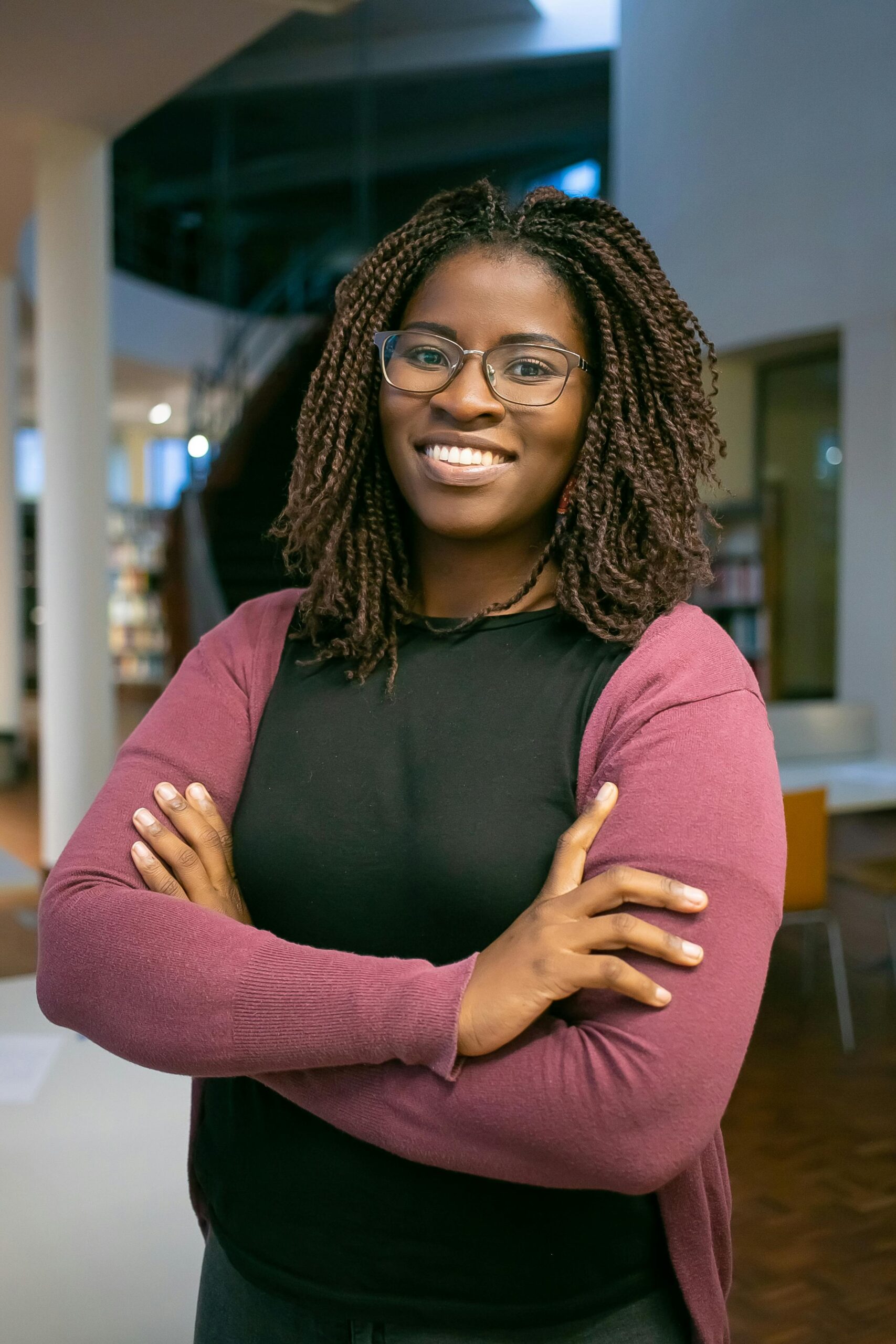 Portrait of woman smiling A smiling woman standing in a library. Behind her are stairs and shelves of books.